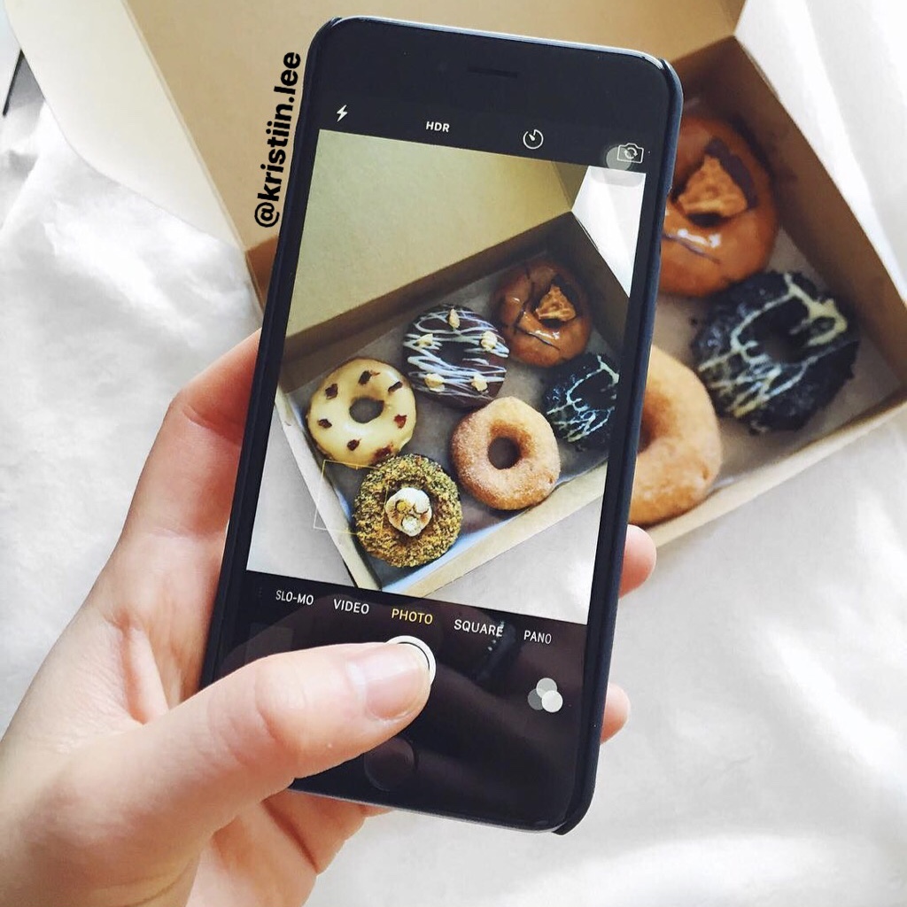 Hand holding an iPhone taking a photo of donuts